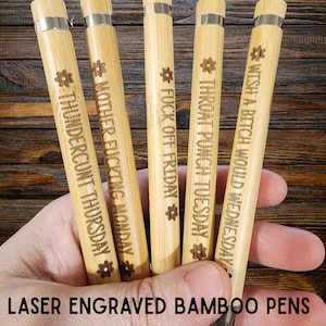 May include: Five bamboo pens with laser-engraved text, including phrases like "THUNDERCUNT THURSDAY" and "FUCK OFF FRIDAY." Each pen has a silver metal band and a natural wood finish. The text "LASER ENGRAVED BAMBOO PENS" is at the bottom.