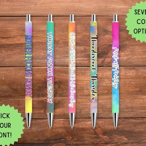 以下が含まれることがあります： 仕事の各曜日のユーモラスなフレーズが書かれた5本のカラフルなペン。ペンはグラデーションデザインで、先端はシルバーです。「Mother Fucking Monday」、「Throat Punch Tuesday」、「Wish a Bitch Would Wednesday」、「Thundercunt Thursday」、「Fuck off Friday」の文字が含まれています。