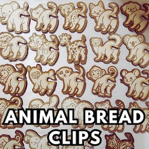 May include: Wooden animal-shaped bread clips featuring various animals like elephants, cats, and giraffes. The clips are light brown with etched details and a slot for securing bread bags. The text "ANIMAL BREAD CLIPS" is displayed.