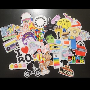May include: A collection of colorful stickers with 1980s pop culture themes. Designs include a Rubik's Cube, a boombox, a cassette tape, a smiley face, and the text "I 80s". Other stickers feature characters and logos.
