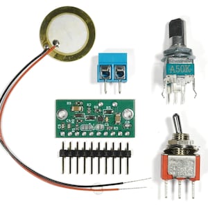 Op de afbeelding: Een verzameling elektronische componenten, waaronder een goudkleurige piëzo-schijf met draden, een blauwe klemmenblok, een groene printplaat, een potentiometer en een rode tuimelschakelaar. De componenten zijn op een witte achtergrond geplaatst.