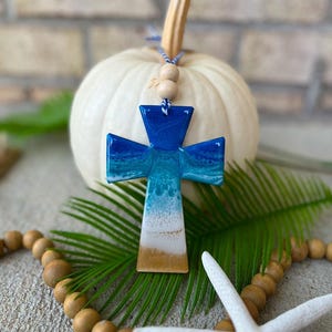Handmade cross ocean resin ornament resting on a white pumpkin, coastal-inspired design with ocean waves