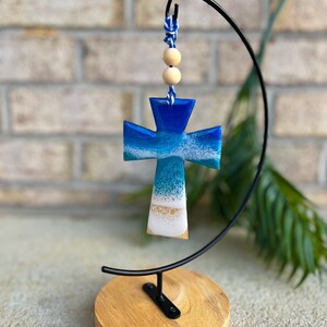 Cross shaped wooden ornament with resin ocean waves on the front on an ornament hanger