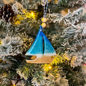 Handmade Sailboat shaped wooden ornament featuring ocean resin waves, finished with blue and white twine and two natural wooden beads