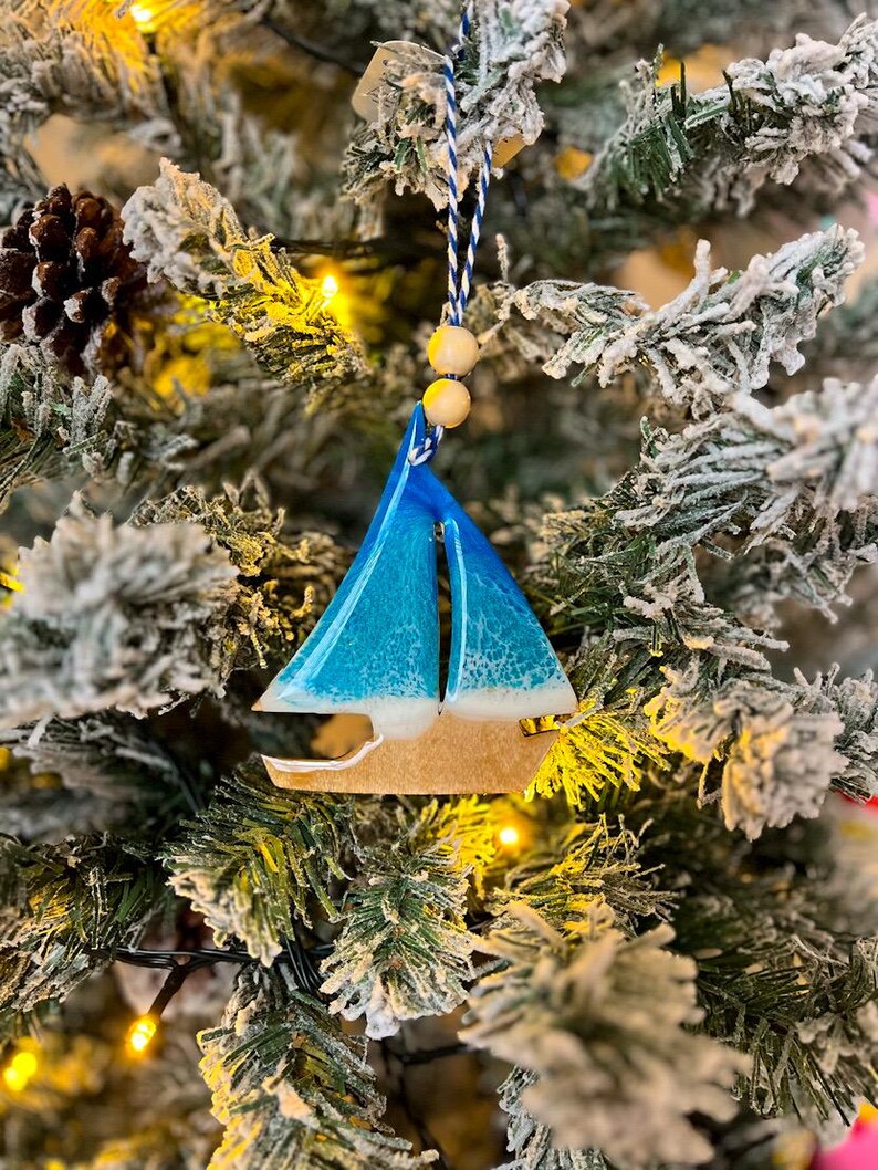 Handmade Sailboat shaped wooden ornament featuring ocean resin waves, finished with blue and white twine and two natural wooden beads