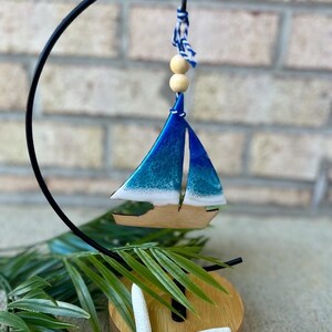 Pode incluir: Um ornamento de veleiro azul e branco com uma base de madeira e uma estrela do mar branca. O ornamento est&aacute; pendurado em um suporte de metal preto.