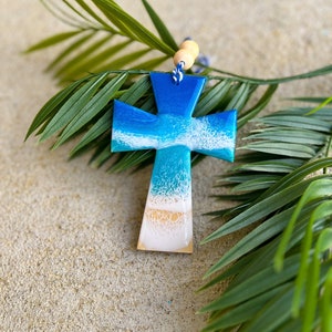 Cross ornament with ocean resin art laying against palm leaves.