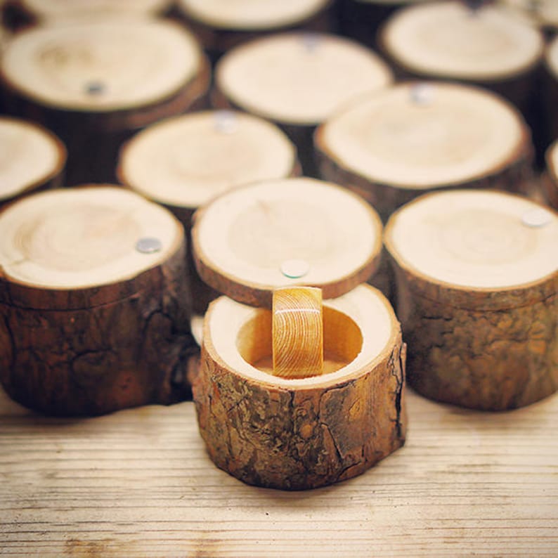 May include: A wooden ring box made from a tree trunk with a ring inside. The box is open and the ring is visible. The box is surrounded by other wooden boxes.