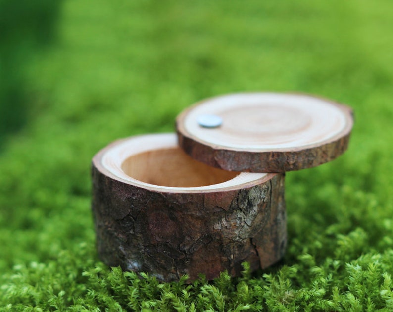 May include: A small wooden ring box made from a tree branch with a natural bark finish. The lid is open and the inside is empty.