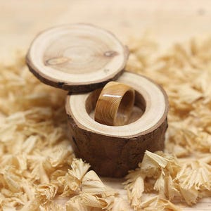 May include: A wooden ring box with a lid, made from natural wood with bark still attached. The box is open and a wooden ring is inside. The ring is made from a light wood with a natural grain pattern.