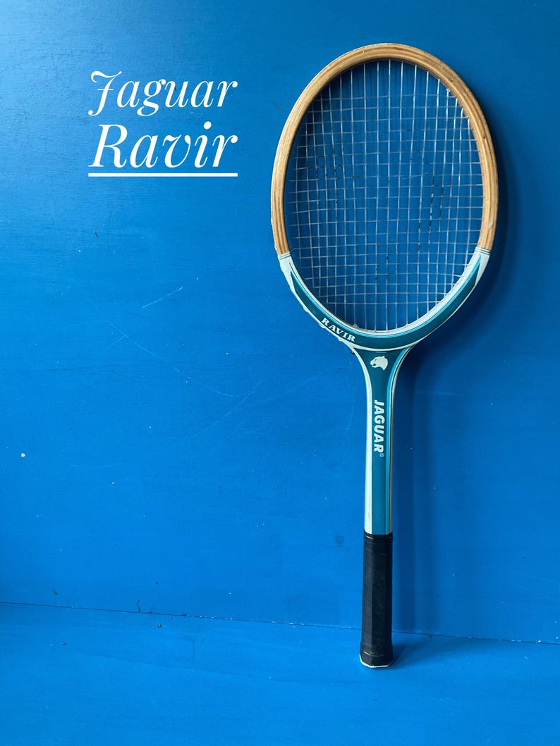 A vintage wooden tennis racket by Jaguar. The racket has a blue and white shaft, with natural wood coloured head. It has a dark handgrip, and is photographed against a blue background
