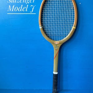 A vintage Slazenger Model J wooden tennis racket. The racket is a faded olive green, with the slazenger logo in red. The top half of the racket head is in natural wood. The racket has a dark leather hand grip