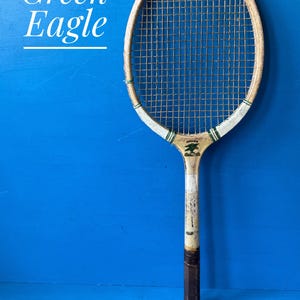 A vintage Green Eagle wooden tennis racket from the 1950s. The racket is predominantly white. There is a picture of a green eagle on the racket face
