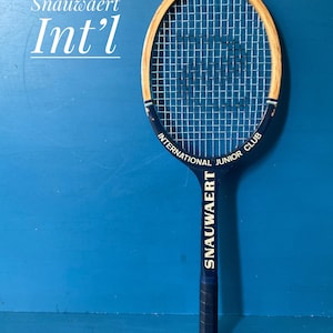 A vintage wooden Snauwaert tennis racket. The racket is has a dark blue handle, with a natural wood head.