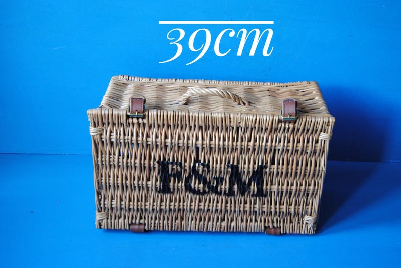 39cm Fortnum and Mason willow picnic basket. The basket is sitting upright, with the Fortnum and Mason logo facing front. The basket has an integrated willow handle, plus a hinged lid that has two leather straps to hold the lid securely in-place