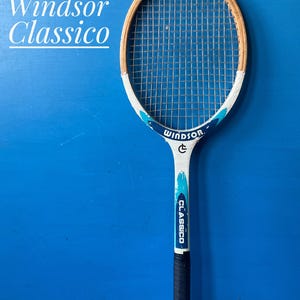 A Windsor Classico tennis racket featuring a natural wood frame head, white throat and shaft with teal and dark blue accents, and a black grip. The text Windsor Classico is printed on the frame and appears in the image background.
