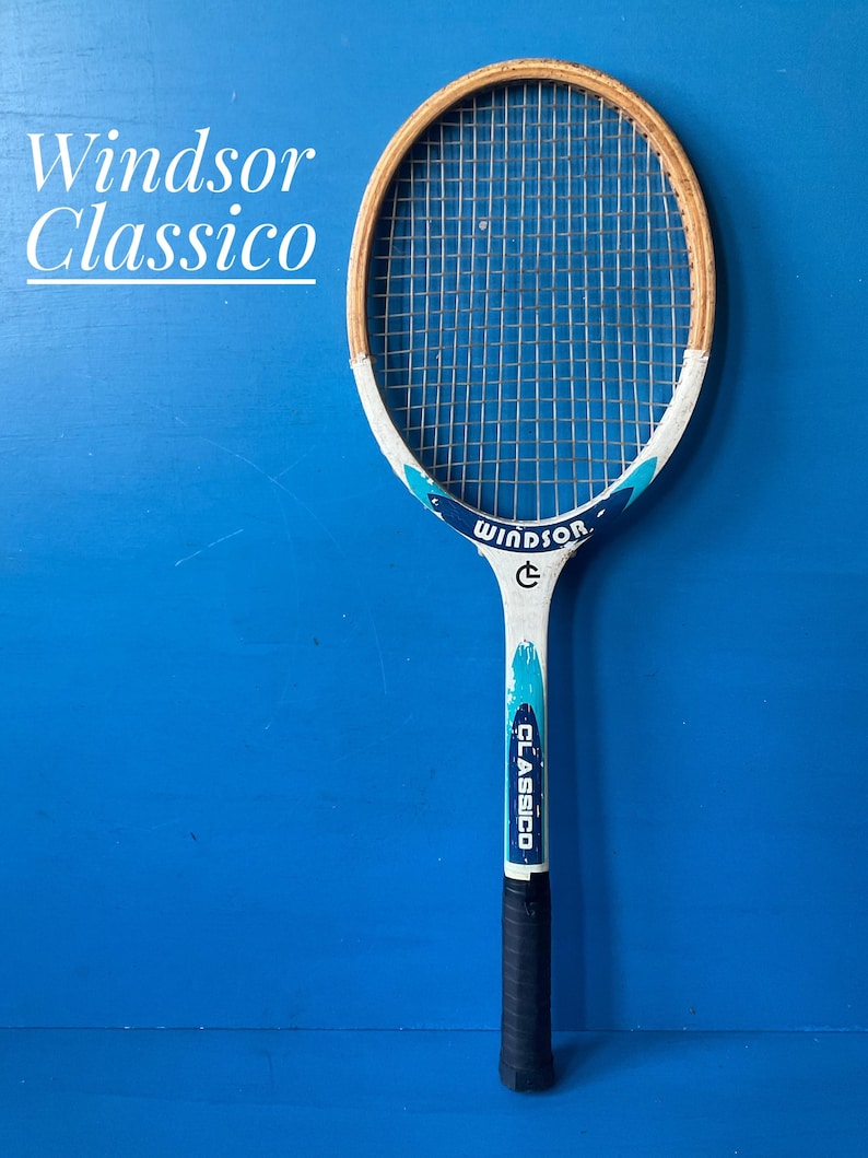 A Windsor Classico tennis racket featuring a natural wood frame head, white throat and shaft with teal and dark blue accents, and a black grip. The text Windsor Classico is printed on the frame and appears in the image background.