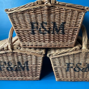 Three Fortnum and Mason Huntsman style wicker baskets with bi- fold lids and wicker handle. The baskets are stacked, with the F&M logo facing forward