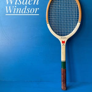 A vintage wooden tennis racket featuring a light wood frame, white throat, and a brown leather grip. The racket includes a red logo and the text "Wisden" and "Windsor" on the frame. The text "Wisden Windsor" is also visible in white.