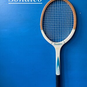 A vintage wooden tennis racket by Sondico. The racket is white, with blue flashes. It has a dark coloured leather hand grip