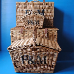 Selection of empty Fortnum and Mason wicker hamper baskets for home storage, from XL to mini huntsman. The baskets all feature the Fortnum and Mason logo in black, visible from the front.