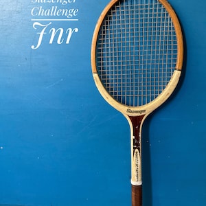 A vintage wooden tennis racket with a natural wood frame, white painted accents, and a brown leather grip. The racket features the text Slazenger Challenge Jnr printed on the frame and the head, with a standard nylon string pattern.