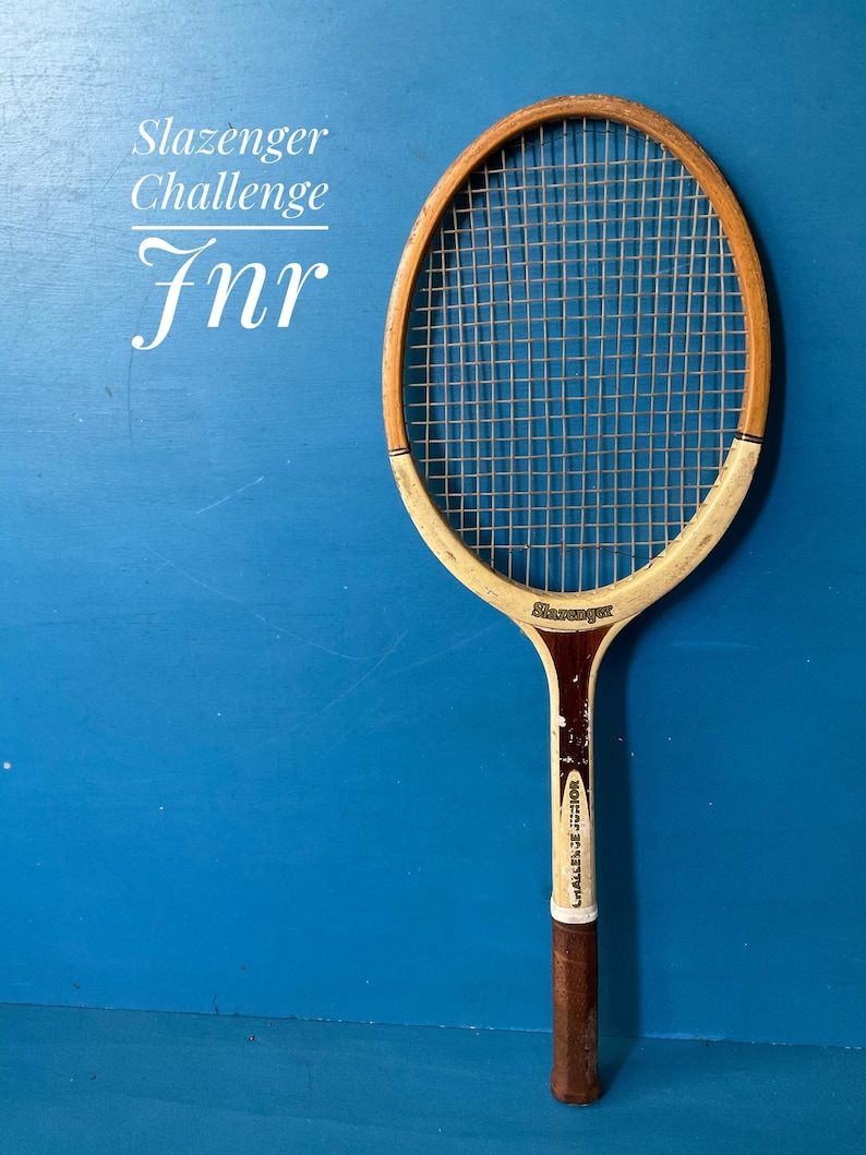 A vintage wooden tennis racket with a natural wood frame, white painted accents, and a brown leather grip. The racket features the text Slazenger Challenge Jnr printed on the frame and the head, with a standard nylon string pattern.