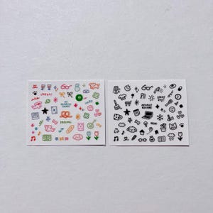 May include: Two white square stickers with colorful and black doodles. One sticker has doodles in color with text like "LIVEYAS" and "MY FAVORITE THINGS". The other sticker has black doodles with text like "MY DAILY ROUTINE" and "Sunny day!"