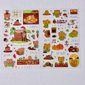 May include: Two sheets of stickers featuring cartoon bears in various poses, interacting with nature elements like mushrooms, carrots, and tree stumps. The stickers have Korean text and a "Earth Energy" graphic.