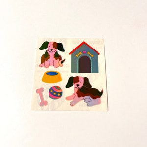 May include: A sheet of stickers featuring a dog house, a dog bowl, a bone, a ball, and two dogs. The stickers are on a white background.