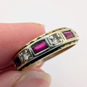 May include: A silver and gold band ring with a row of rectangular ruby stones and two smaller clear stones.