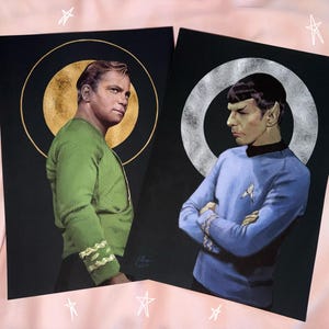 May include: Two rectangular art prints featuring portraits of Star Trek characters. One print shows a figure in a green uniform with a gold circular halo, while the other shows a figure in a blue uniform with a silver circular halo, both on black backgrounds.