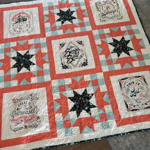 May include: A handmade quilt with a patchwork design. The quilt features coral, white, and light blue squares and star patterns. Each square contains floral text. The quilt is a cozy home decor item.