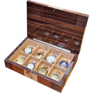 May include: Open wooden watch box with a glossy finish, showcasing nine pocket watches. The box is made of dark brown wood with lighter wood accents. The watches have various designs and colors, including gold, silver, and blue.