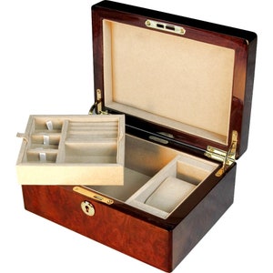May include: A dark wood jewelry box with a hinged lid and a lock. The interior is lined with beige velvet and has compartments for rings, earrings, and a watch.
