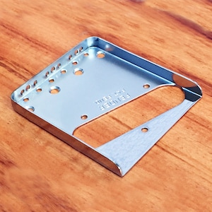 May include: A silver-coloured metal guitar bridge plate with the text "Fender Pat. Pend." engraved on the surface.