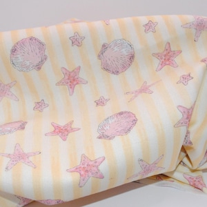 May include: A piece of fabric featuring a repeating pattern of pink starfish and seashells printed over a background of vertical pale yellow and white stripes. The textile has a soft, draped appearance with visible folds across the surface.
