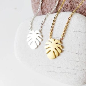 Puede incluir: Dos delicados collares con un colgante de hoja tropical. Un collar es plateado y el otro es dorado.