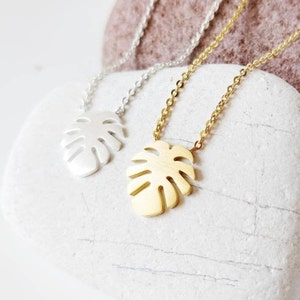 Puede incluir: Dos delicados collares con un colgante de hoja tropical. Un collar es plateado y el otro es dorado.