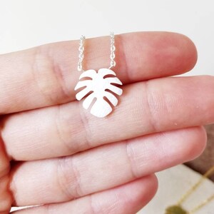 Puede incluir: Un collar de plata con un delicado colgante de hoja de monstera.