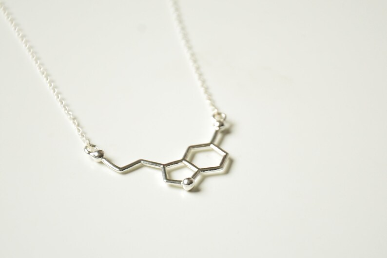 May include: A silver necklace with a pendant shaped like the chemical structure of dopamine.