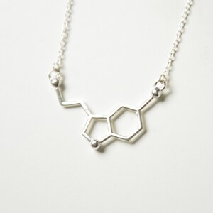 May include: A silver necklace with a pendant shaped like the chemical structure of dopamine.