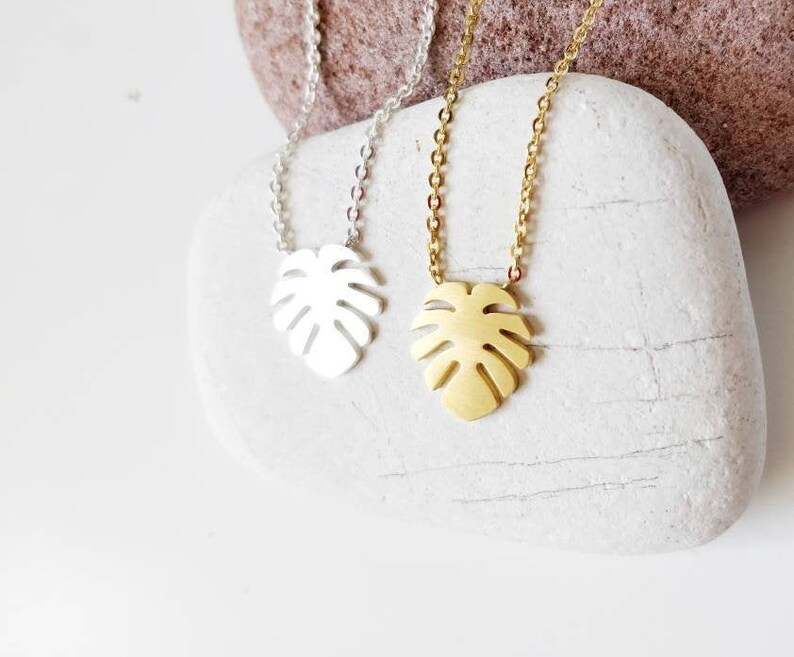 Puede incluir: Dos delicados collares con un colgante de hoja de monstera. Uno es de oro y el otro de plata.