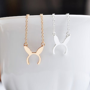 May include: Two delicate necklaces with bunny ear pendants. One necklace is gold and the other is silver.