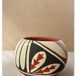 May include: A white ceramic bowl with black and red geometric designs. The bowl has a rounded shape and a smooth surface.