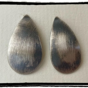 May include: A pair of silver teardrop-shaped earrings with a brushed finish.