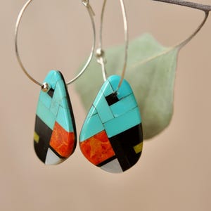May include: A pair of silver hoop earrings with turquoise, red, and black geometric inlay teardrop dangles.