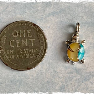 May include: A small silver turtle charm with a yellow and blue shell. The charm is about the size of a US penny.