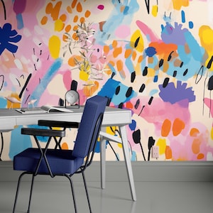 May include: A white desk with a blue chair in front of it. The desk has a lamp with a white shade and a clock on it. The wall behind the desk is painted with a colorful abstract floral pattern.