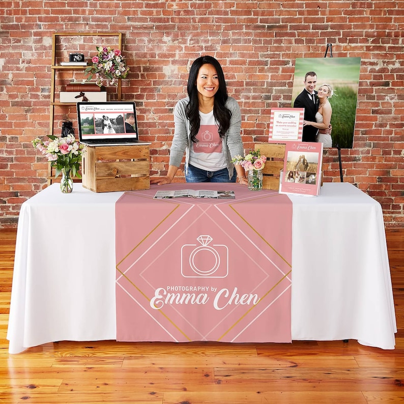 May include: A pink table runner with a gold and white geometric design. The runner features a camera icon with a diamond ring inside and the text "PHOTOGRAPHY by Emma Chen".